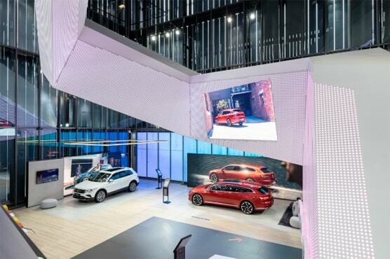 Foto in den Ausstellungsraum im VW Pavillon. Zwei Modelle stehen unterhalb einer futuristischen Treppe. Drum herum Aufsteller und Bildschirme.