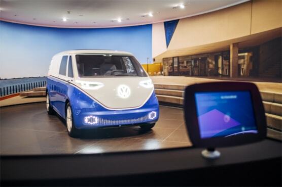 Foto in den VW Nutzfahrzeuge Pavillon. Auf der Ausstellungsfläche parkt ein grau-blaues Modell neben Treppen.