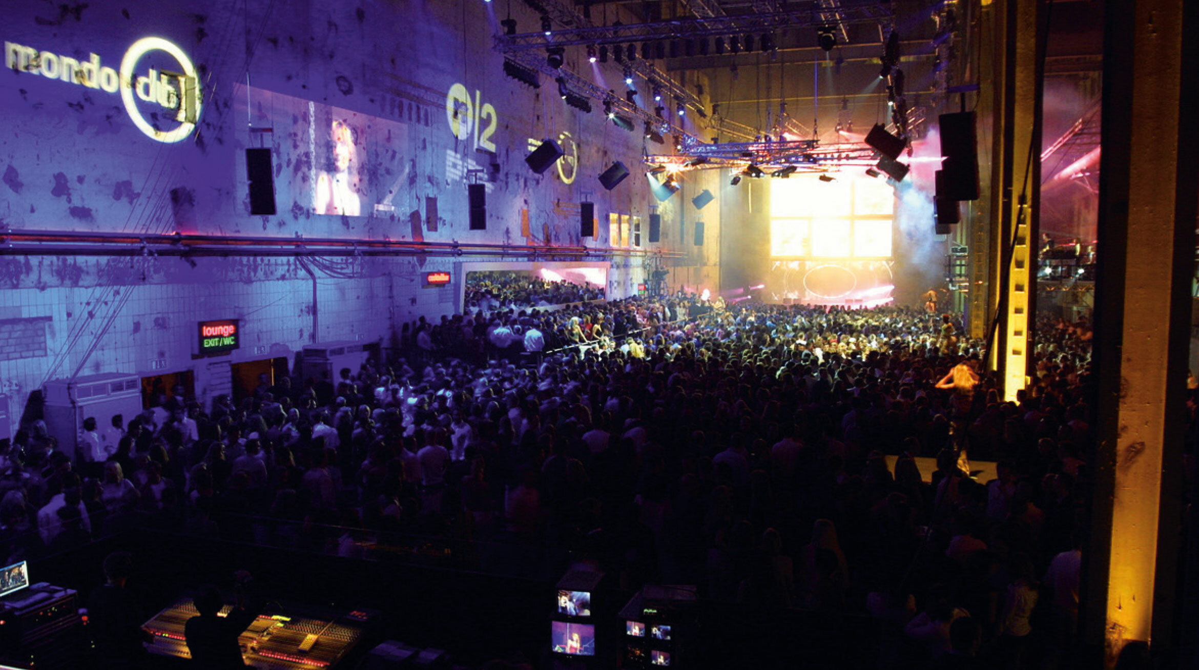 Foto eines Events in der Autostadt. Eine mit Menschen gefüllte Halle ist in lilafarbenes Licht getaucht. Die Menschen wenden sich zu einer Bühne.
