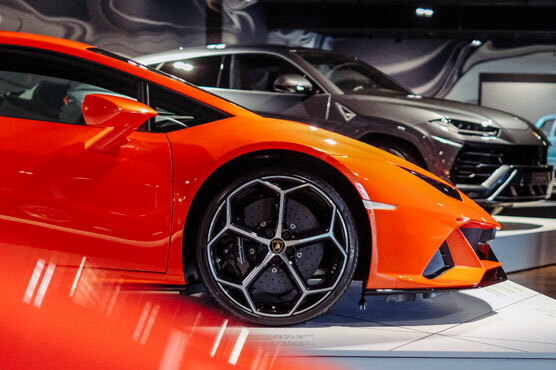 Nahaufnahme des rechten Vorderreifen und der filigranen Felgen eines orange-roten Lamborghini, der neben einem grauen-silbernen Modell steht.