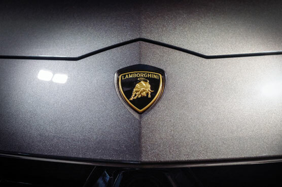 Nahaufnahme des Lamborghini Emblems auf einem silber-grauen Wagen. Ein goldener Stier auf schwarzem Untergrund.