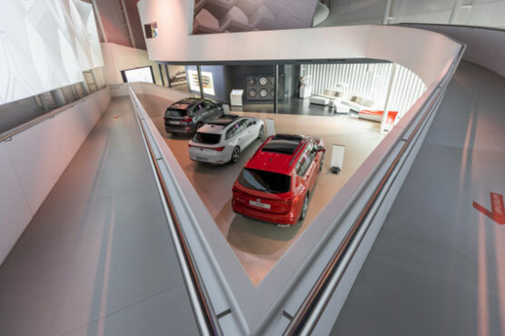Foto in den Ausstellungsraum des Seat Pavillon. 3 Seat Wagen – rot, grau und schwarz – sind nebeneinander vor einer Lounge geparkt.