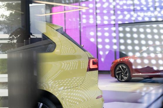 Bild in den VW Pavillon. Zu sehen sind zwei Modelle hinter einer Glasscheibe und Lichtpunkt-Projektion in einem lilafarbenen Raum.