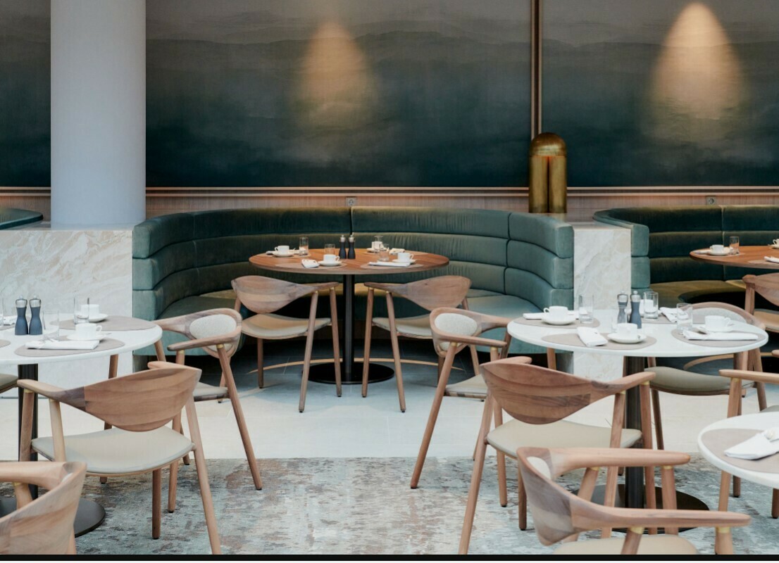 Foto der Frühstücklounge, gedeckte Tische und bepolsterte Sitzecken. Die Wand bildet eine große Malerei in Blautönen.
