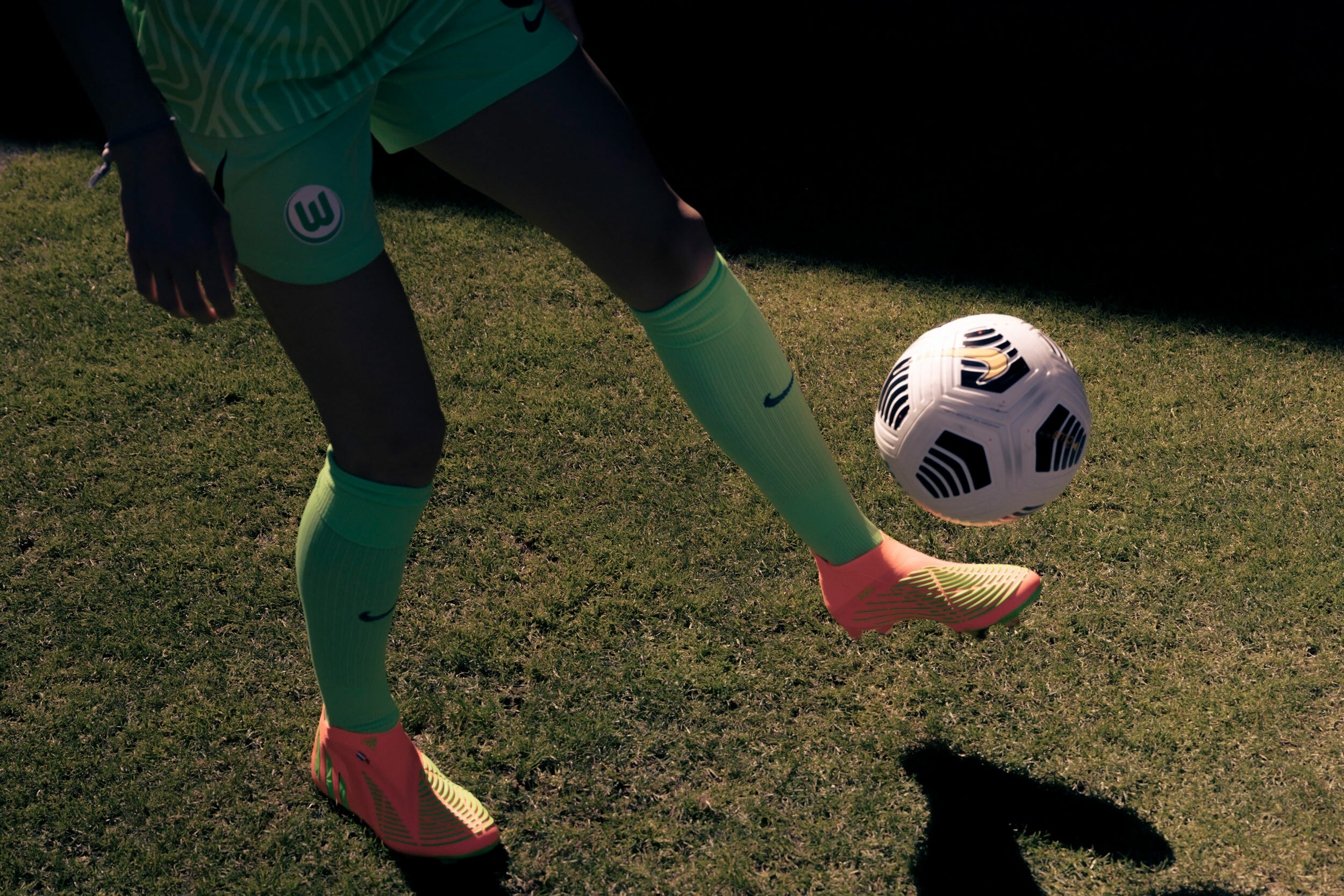 Nahaufnahme auf die Füße von Fußballerin Dominique Janssen. Mit Stollenschuhen steht sie auf einem Rasen und kickt einen Fußball mit dem linken Fuß.
