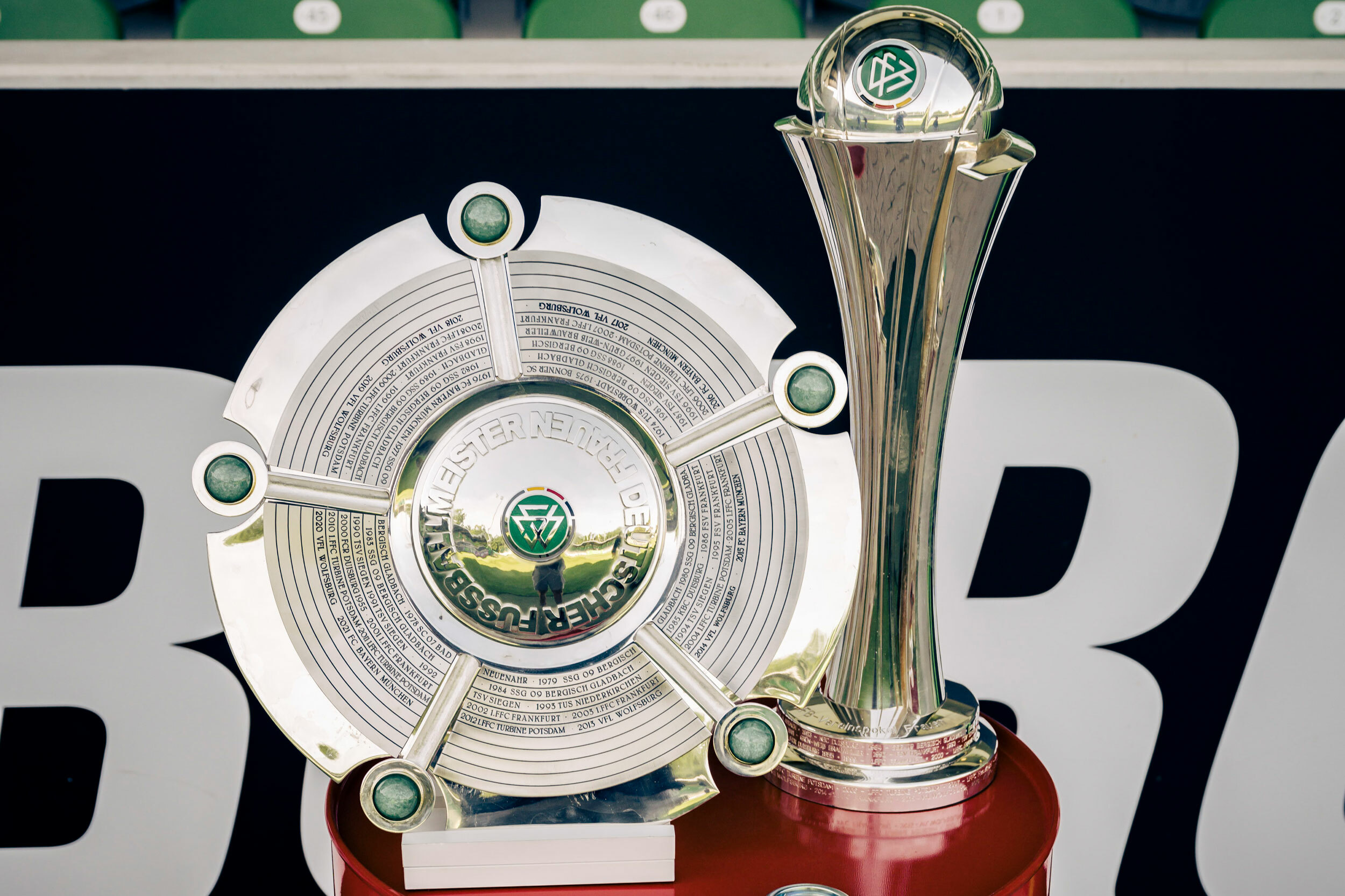 Nahaufnahme eines silbernen Pokals neben einer silbernen Meisterschale, auf der "Deutscher Fußballmeister Frauen" steht.