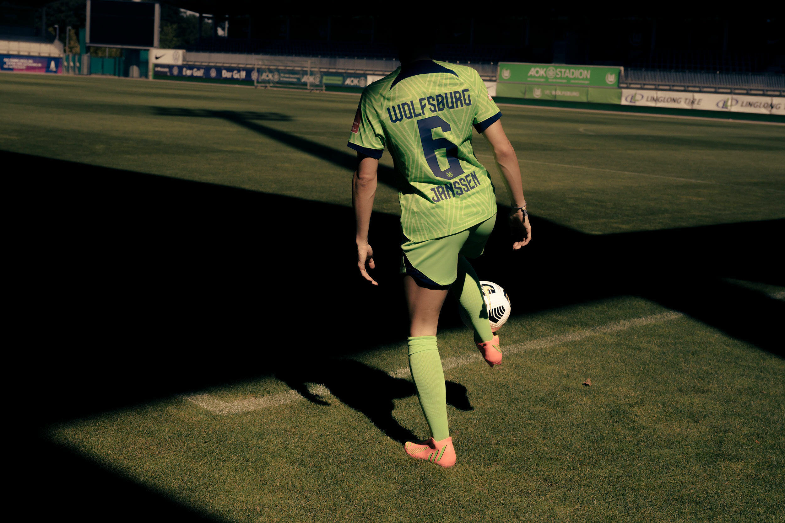 Rückansicht von Dominique Janssen beim Tribbeln. Die Fußballerin trägt ein grünes Trikot mit der Nr. 6 und lupft einen Ball.