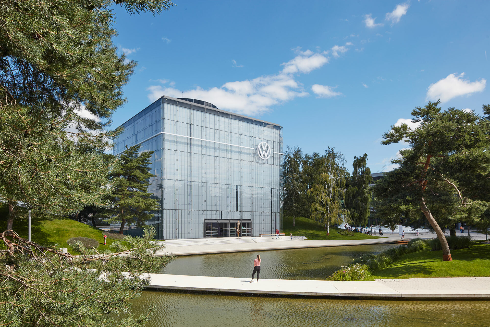 Foto des VW Pavillon in der Autostadt. Das quadratische Gebäude ist von Bäumen und Wasser gesäumt.