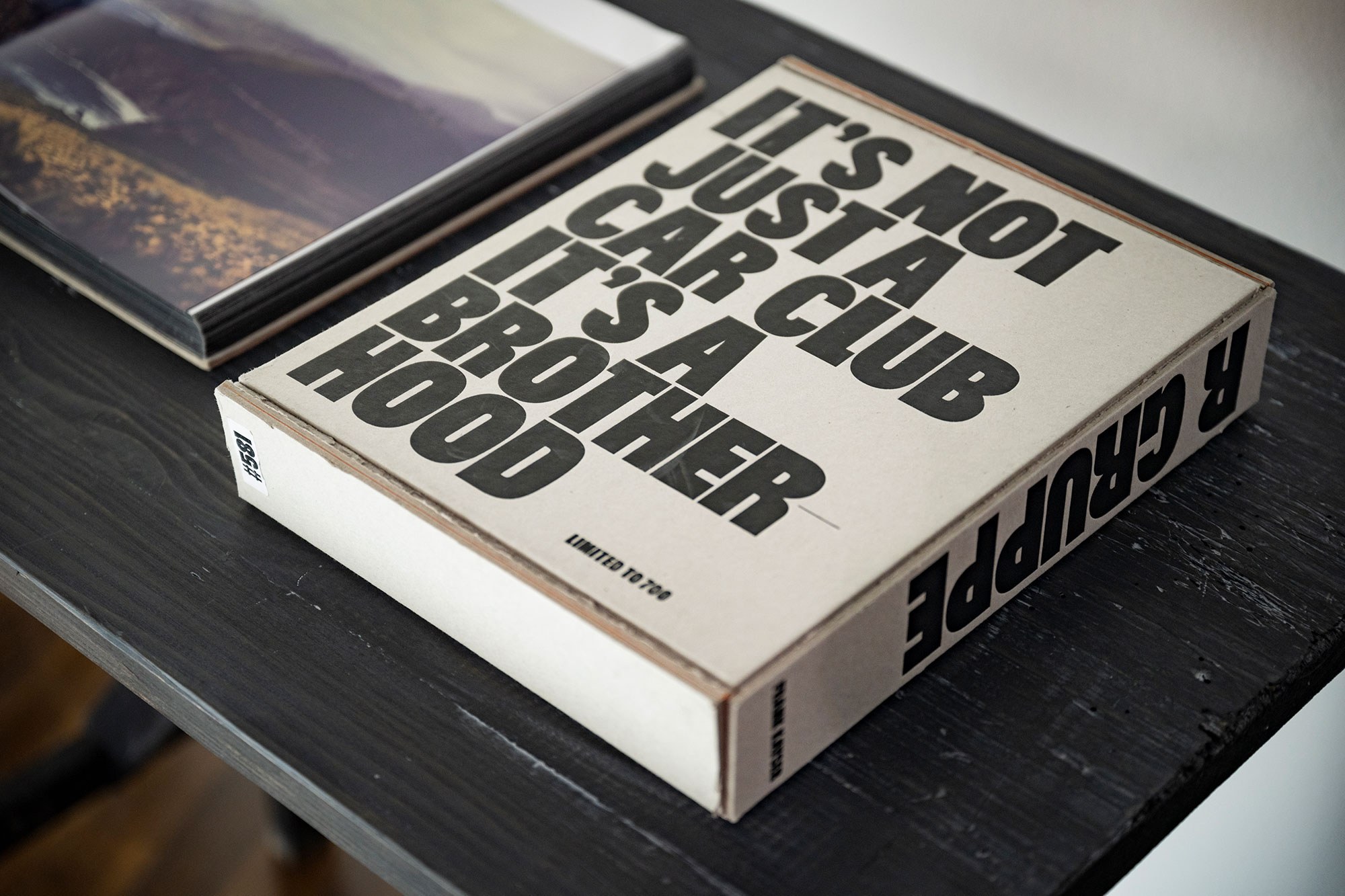 Foto eines Buches mit dem Titel "Its not just a car club its a brotherhood", neben einem anderen Buch auf schwarzem Tisch liegend..