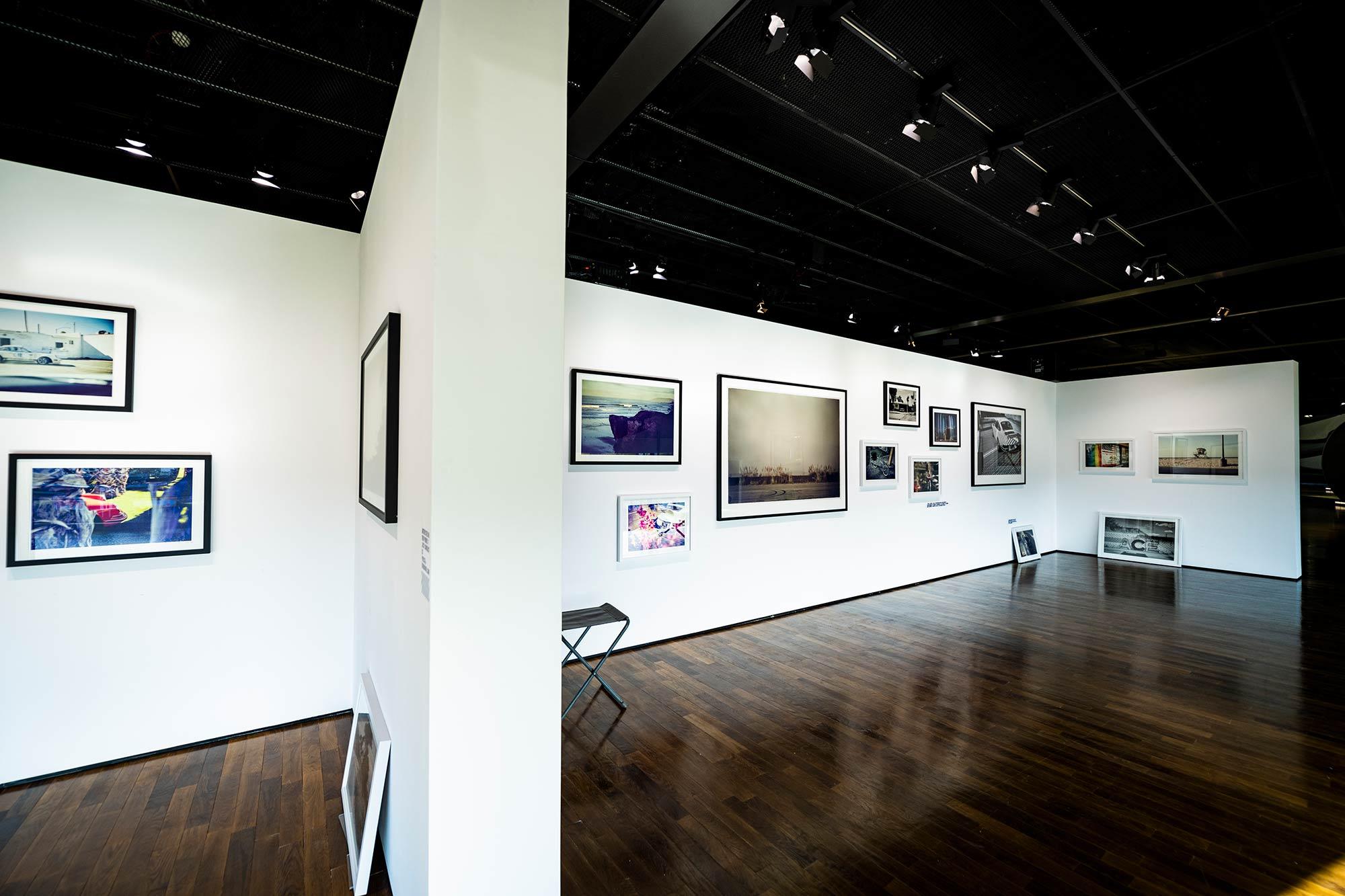 Fotografie in einen Ausstellungsraum. Zu sehen sind weiße Wände, an denen gerahmte Fotografien hängen und lehnen.