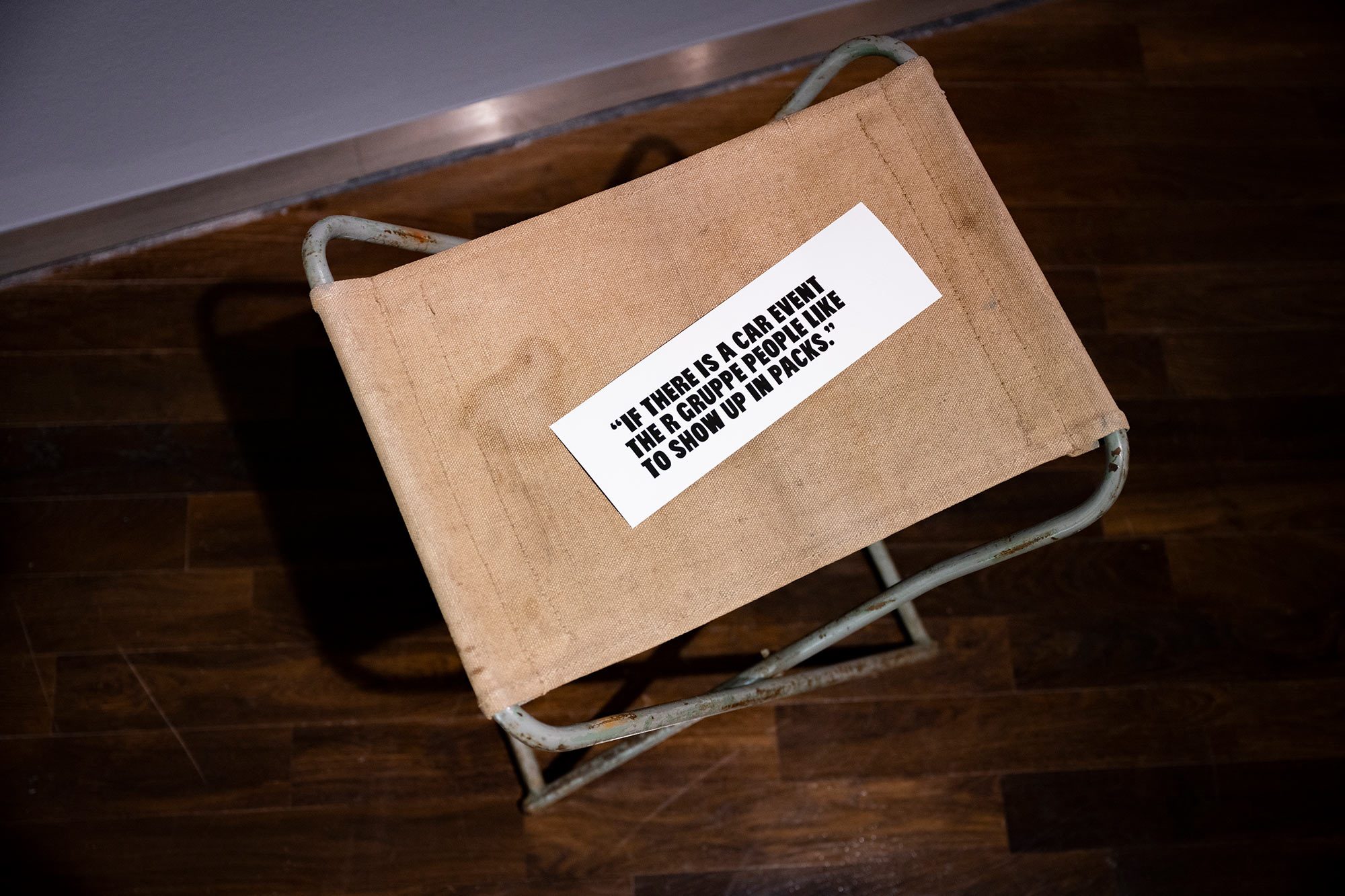 Fotografie eines rostigen Klappsessels mit beiger, fleckiger Sitzfläche. Darauf liegt ein Zitat, das auf ein weißes Papier gedruckt ist.