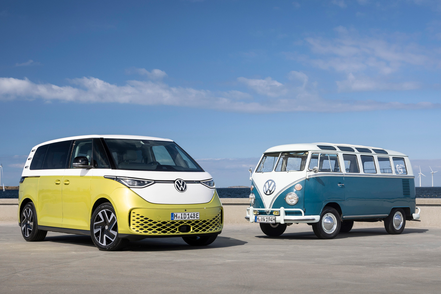 Foto von zwei VW-Bullis. Links im Bild parkt ein gelb-weißes Modell. Diesem zugewandt steht rechts ein blau-weißes Modell.