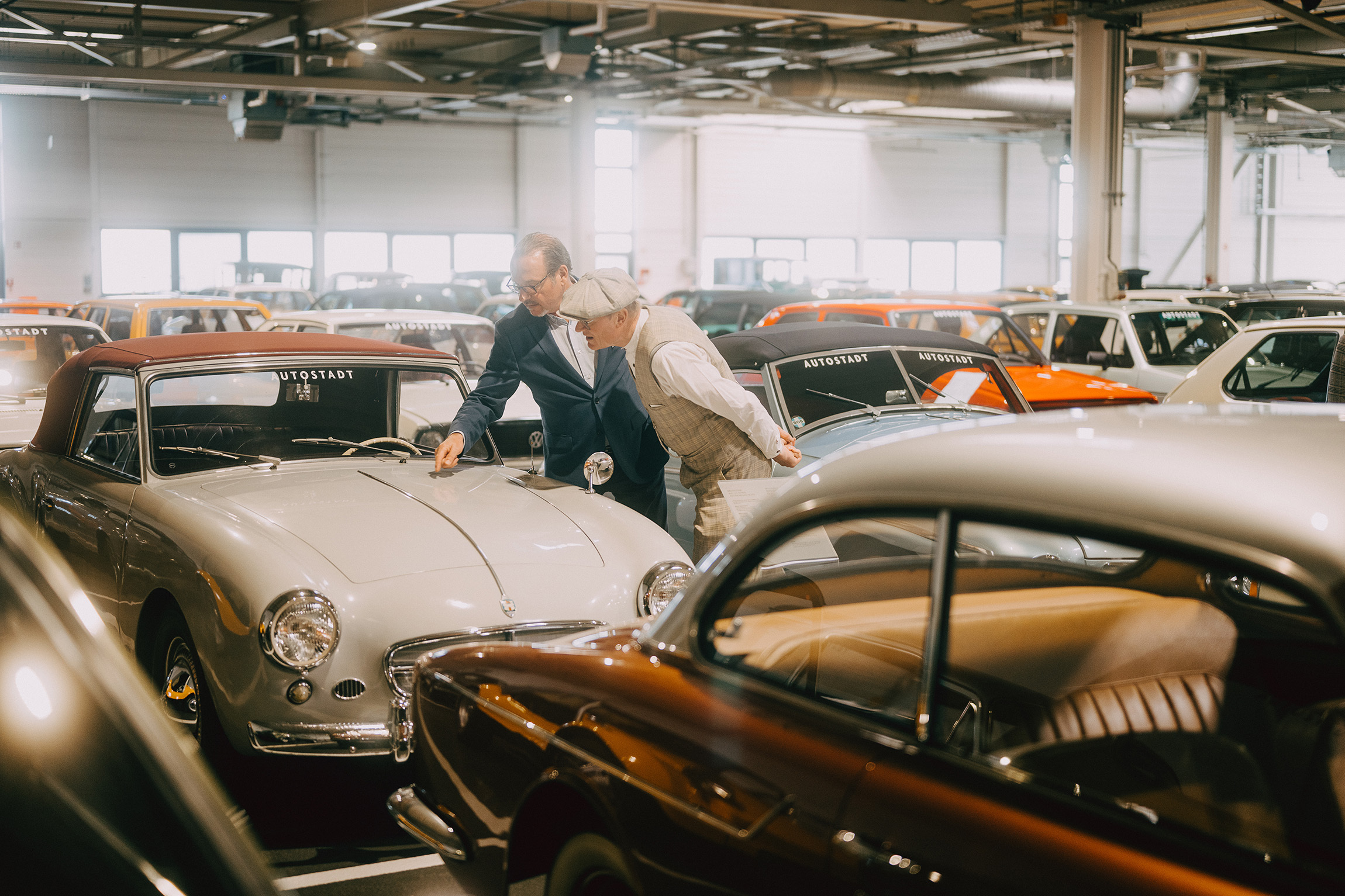 Foto von zwei Menschen, die in einem musealen Ausstellungsraum stehen und sich inmitten von historischen Autos über eine Motorhaube beugen.